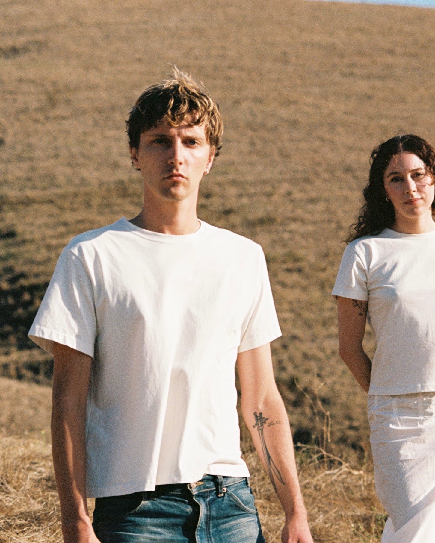 Two people wearing white t-shirts standing in a dry, open field.